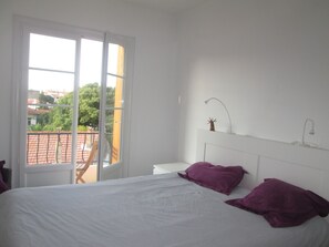 Une chambre à coucher avec un lit, deux oreillers, une table de chevet, une lampe et une fenêtre donnant sur des bâtiments et des arbres.