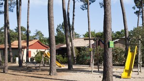 A playground with slides and swings, surrounded by trees and buildings. - air-conditioned CHALET DE CHARME (Soulac-Sur-Mer)
