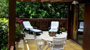 A wooden deck with a table and chairs, surrounded by lush greenery. - air-conditioned CHALET DE CHARME (Soulac-Sur-Mer)