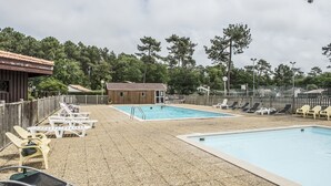 A pool area with lounge chairs, a small building, and a fenced area with trees in the background. - air-conditioned CHALET DE CHARME (Soulac-Sur-Mer)