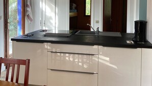 A modern kitchen with white cabinetry, a black countertop, and a wooden dining table. - air-conditioned CHALET DE CHARME (Soulac-Sur-Mer)