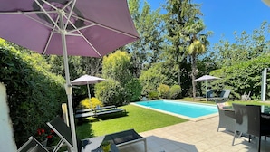 A backyard with a swimming pool, patio furniture, and a pergola with umbrellas.