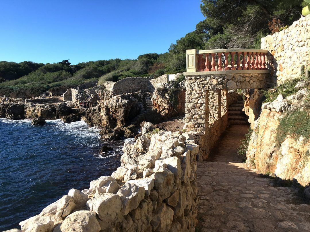 Un sendero de piedra costero que conduce a una barandilla de piedra con vistas al mar.