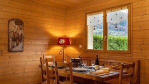 A wooden dining room with a table set for four, a red lamp, and a window with a view of greenery. - LES AMARYLLIS - Le Buet (Taninges)