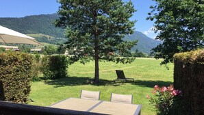 A patio with a table and chairs, a tree, and a view of a grassy field and mountains. - LES AMARYLLIS - Le Buet (Taninges)