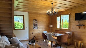 A cozy cabin interior with a wooden dining area, a sofa, and a television mounted on the wall. - LES AMARYLLIS - Le Buet (Taninges)