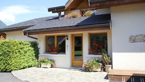 A two-story building with a wooden balcony, large windows with flower boxes, and a stone-paved entrance. - LES AMARYLLIS - Le Buet (Taninges)