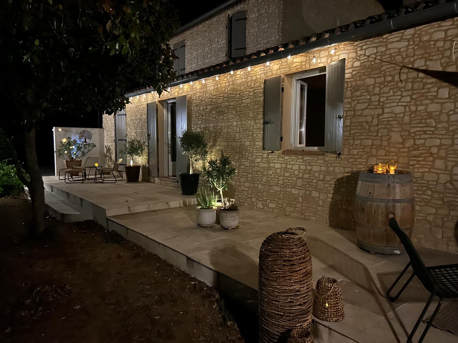 Un espace extérieur aménagé en patio, avec des murs en pierre, des plantes en pot, un tonneau en bois et du mobilier d’extérieur.