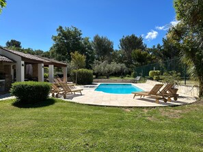 Un patio trasero con piscina, sillas de descanso y una pérgola.