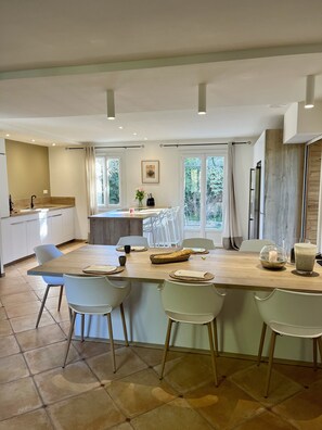 Una cocina moderna con una isla central, sillas blancas y una mesa de comedor preparada para cuatro comensales.