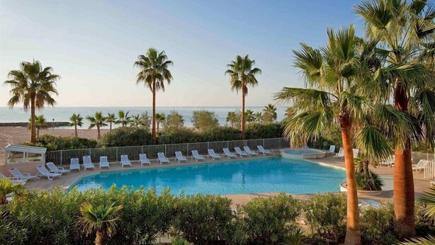 A pool with lounge chairs and palm trees, overlooking a beach.