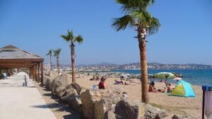 A beach with palm trees, a covered walkway, and people relaxing.