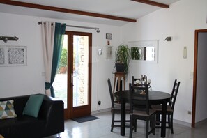 A room with a dining table, chairs, a sofa, a potted plant, and a door leading to an outdoor area.