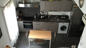 Una cuina compacta amb electrodomèstics moderns, una zona de menjador amb taula i cadires, i una escala que condueix a un nivell superior.