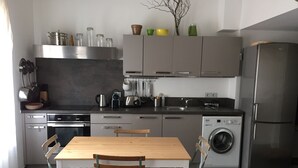 Una cuina moderna amb electrodomèstics d'acer inoxidable, una taula de dinar de fusta i una rentadora.