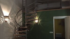 Gescales de caragol amb barana metàl·lica i graons de fusta, a prop d'una paret amb dues làmpades penjades.