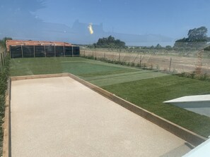 A backyard with a lawn, a concrete play area, and a fenced area with a building in the background.