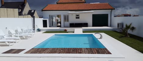 A modern house with a swimming pool, white walls, and a red-tiled roof.