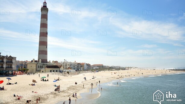 A beach with a tall lighthouse, sandy shore, and buildings in the background. - House Aveiro heated pool (Gafanha do Carmo)