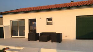 A modern house with a tiled roof, a large sliding glass door, and a patio with outdoor furniture. - House Aveiro heated pool (Gafanha do Carmo)