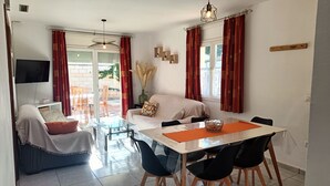 A modern living room with a sofa, dining table, and chairs. There is a TV on the wall, a window with curtains, and a ceiling light. - House with private pool for 5 poeple at 1500 m from the beach in L'Escala (L'Escala)