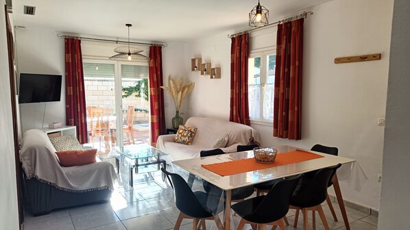 A modern living room with a sofa, dining table, and chairs. There is a TV on the wall, a window with curtains, and a ceiling light. - House with private pool for 5 poeple at 1500 m from the beach in L'Escala (L'Escala)
