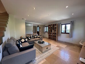 A modern living room with a sofa, a coffee table, a bookshelf, and a staircase. - Villa 200 m from Lake Annecy with terrace and parking (Sévrier)