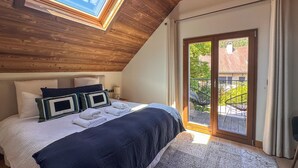 A bedroom with a skylight, a bed with a dark blue bedspread, a large window, and a view of the outside.