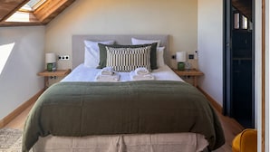 A bedroom with a sloped ceiling, a bed with multiple pillows, bedside tables with lamps, and a wardrobe.