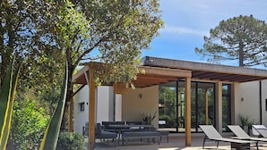 A modern outdoor patio with a wooden deck, seating area, and a pergola.
