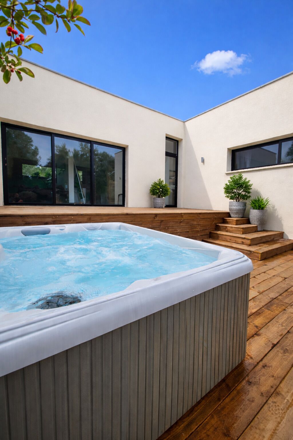Ein moderner Außenbereich mit Whirlpool, Holzterrasse, blauem Himmel und Pflanzen in Töpfen.