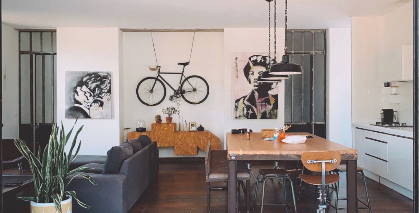 A modern kitchen with a wooden table, bar stools, and a hanging bicycle.