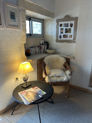 Un coin lecture confortable avec un fauteuil en osier, une petite table avec une lampe et une bibliothèque remplie de livres.