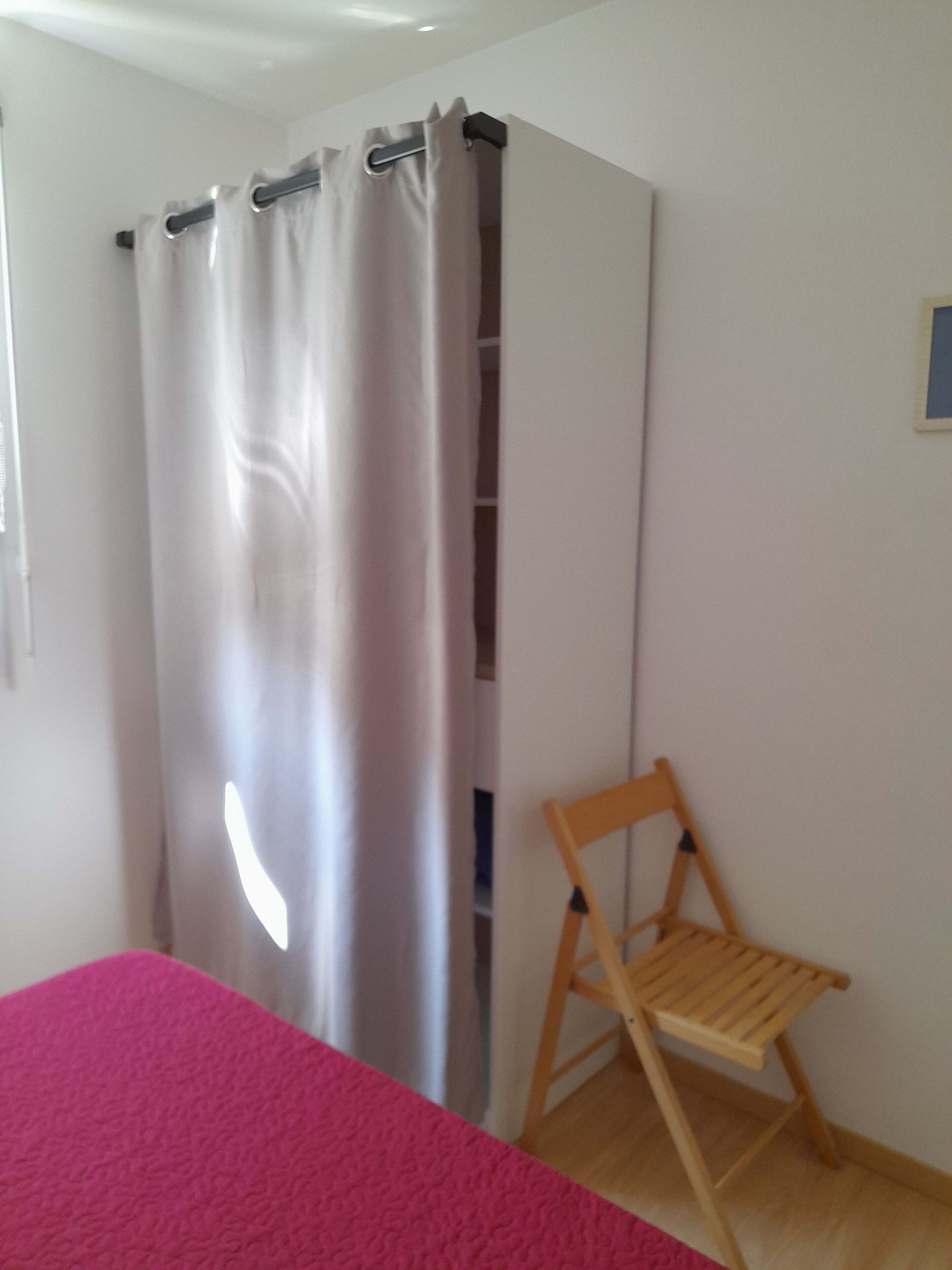 Une pièce avec un lit, une chaise en bois et un rideau.