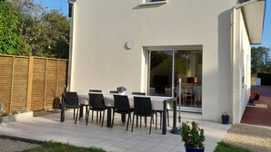 Ein modernes Haus mit weißer Fassade, einem großen Schiebeglastür und einer Terrasse mit Tisch und Stühlen.