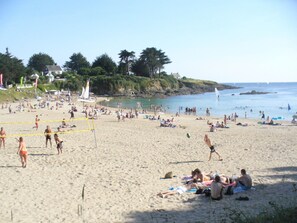 Une plage bondée où les gens se prélassent au soleil et se baignent.