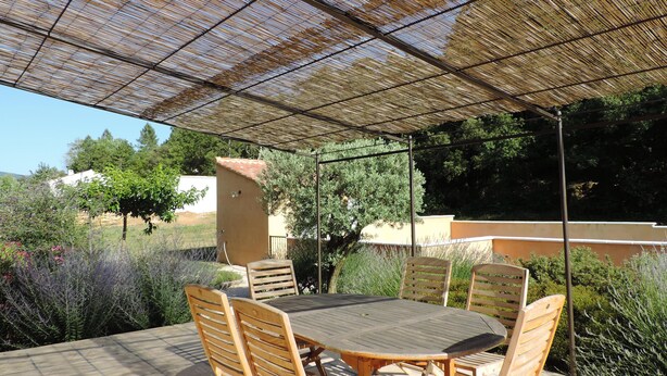 An outdoor patio with a round wooden table and chairs, a pergola overhead, and a view of a residential area with trees and a building in the background. - Bedoin new villa (100m town center) Mont Ventoux, private pool  (Bédoin)