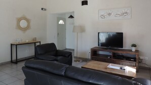 A living room with a black leather sofa, a wooden coffee table, a TV on a wooden stand, a decorative mirror, and a door with a glass panel. - Bedoin new villa (100m town center) Mont Ventoux, private pool  (Bédoin)