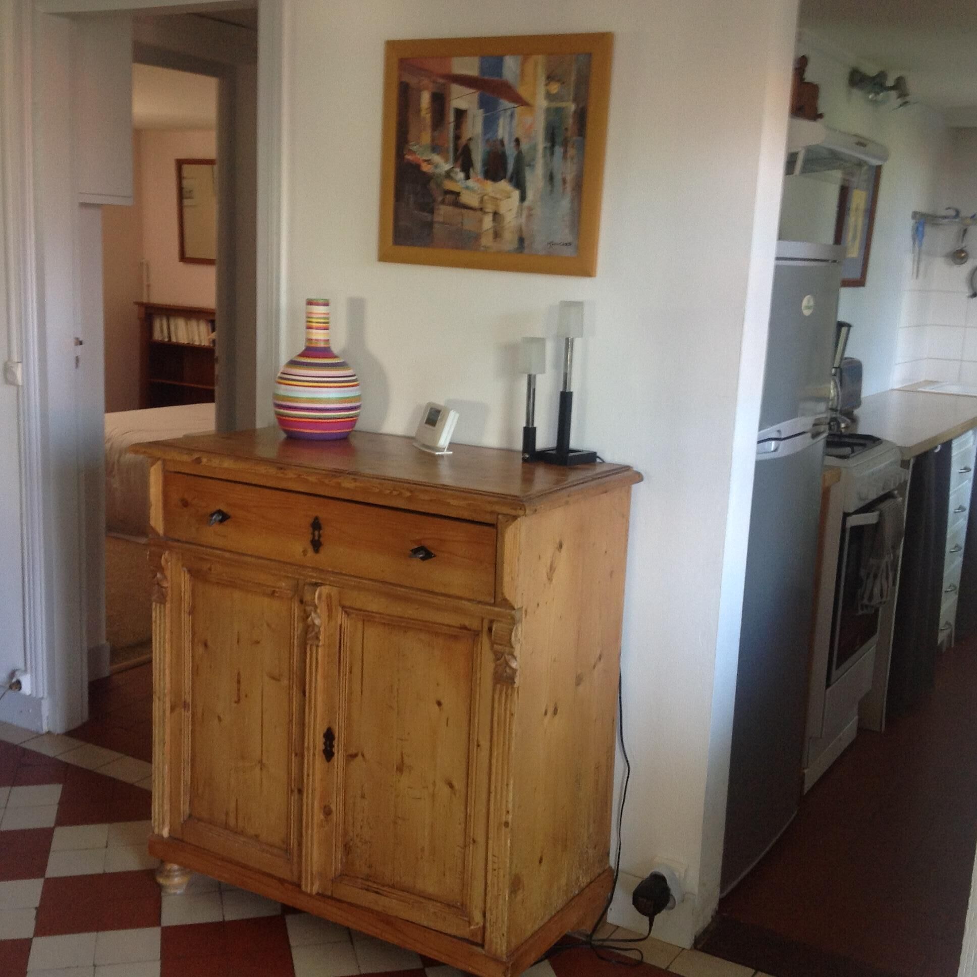 Uma cozinha com um armário de madeira, um vaso colorido e um quadro na parede.