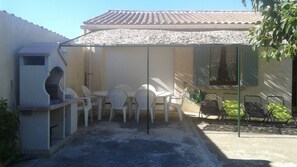 A covered patio with a grill, white plastic chairs, and a table. - Vacation villa in quiet neighborhood near town center (Pernes-Les-Fontaines)