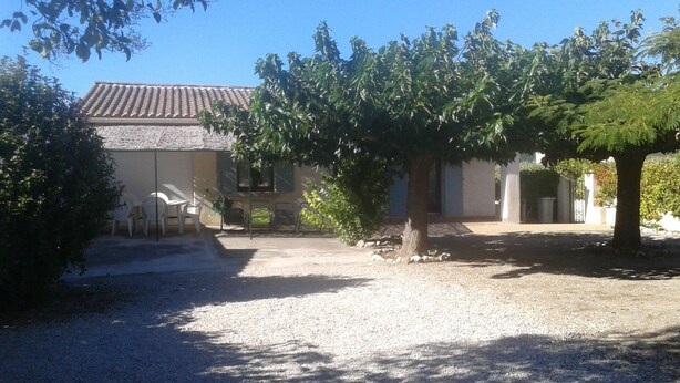 Una casa con techo de tejas, camino de entrada de grava y un árbol en primer plano.