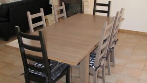 Un comedor con una larga mesa de madera y seis sillas, una chimenea de piedra y un sofá negro al fondo.