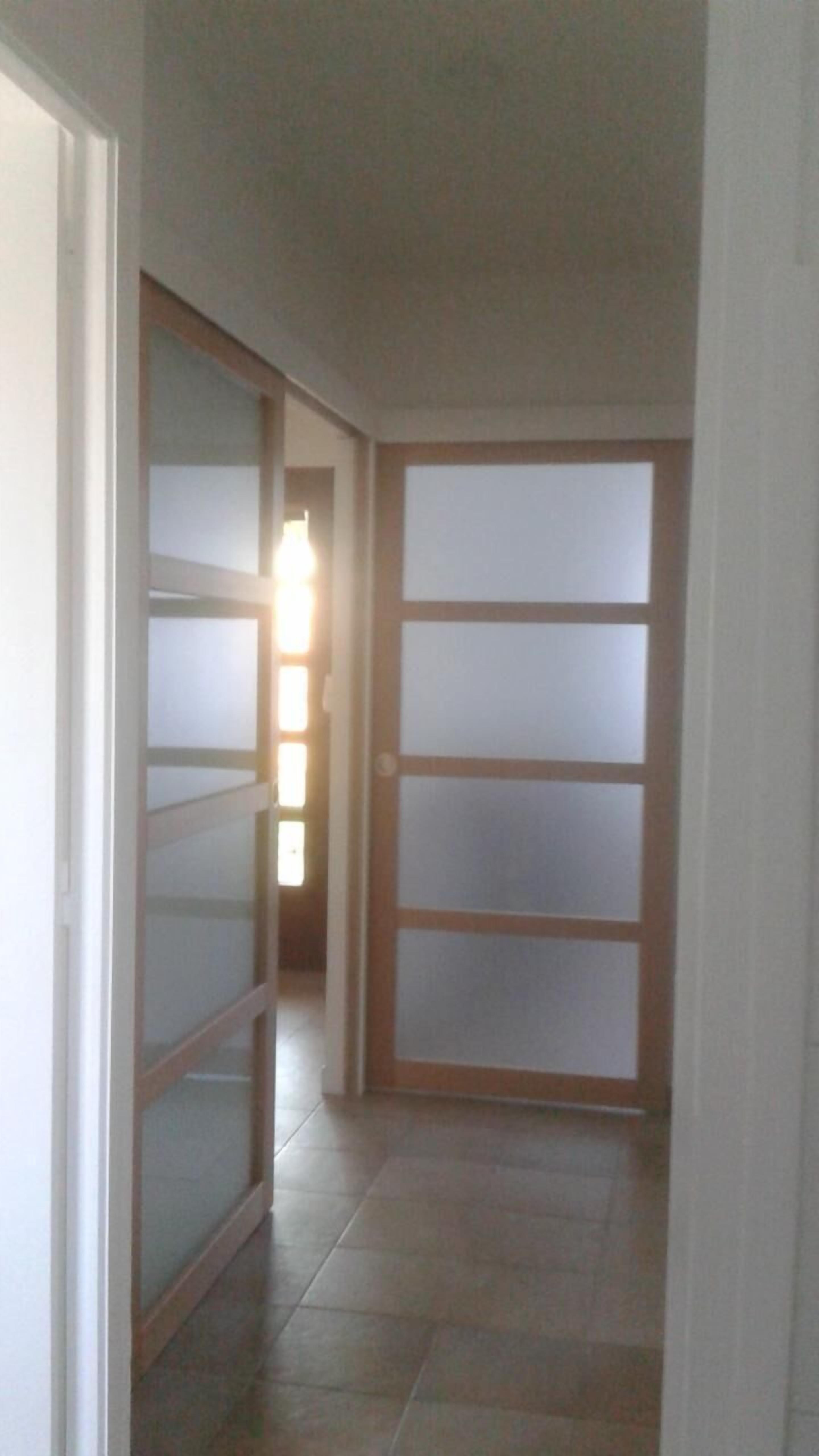Un couloir avec une porte-fenêtre coulissante donnant sur une autre pièce.