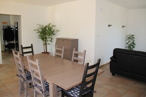A dining area with a wooden table and chairs, a black sofa, and two potted plants. - Vacation villa in quiet neighborhood near town center (Pernes-Les-Fontaines)