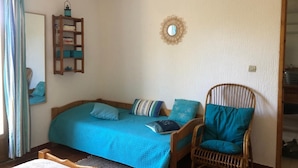 Ein Schlafzimmer mit einem Bett, einem Sessel, einem Spiegel und einem Regal mit Büchern und einer Laterne.