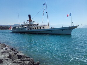 Un barco blanco grande, con varias banderas, amarrado en una costa rocosa.