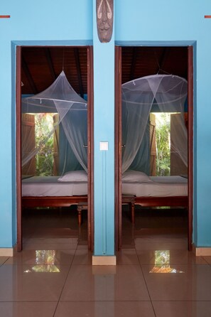 Two wooden beds with mosquito nets, a tiled floor, and a blue wall.