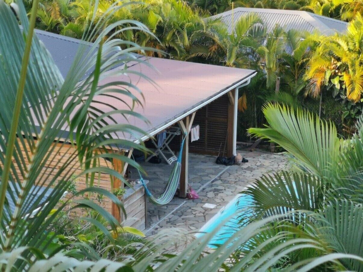 Ein überdachter Außenbereich mit Schwimmbecken, umgeben von üppiger Vegetation und einer Holzkonstruktion.