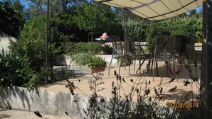 An outdoor patio area with a covered seating area, potted plants, and a view of a building in the background. - Spacious and pleasant house (Castelnau-De-Guers)