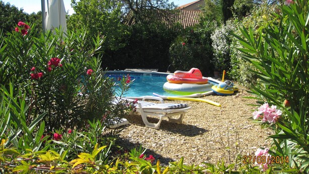 A pool area with inflatable toys, a white umbrella, and a statue. - Spacious and pleasant house (Castelnau-De-Guers)